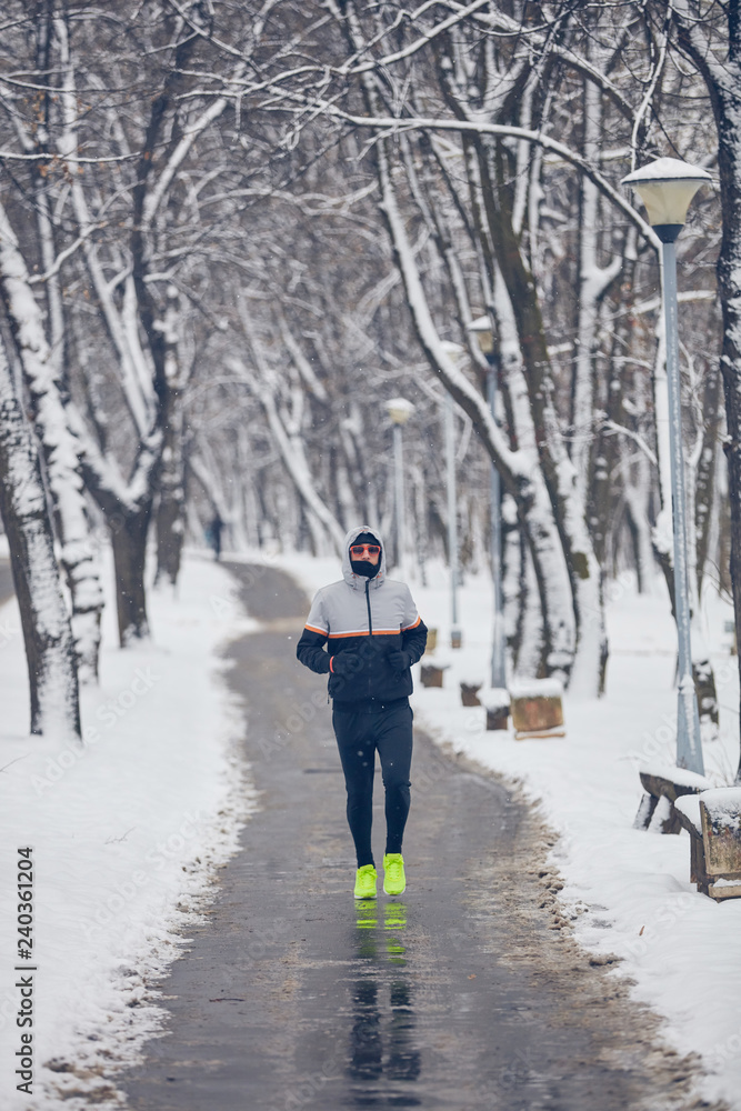 Man jogging in a cold winter snowy day outdoors.