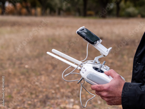 A drone pilot piloting with the remote control with smartphone in his hands in the forest