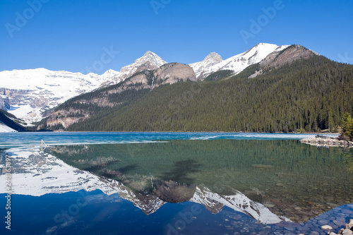 Snowy mountain reflection on half frozen lake Louise - Banff, Alberta, Canada. Shot was taken in late spring.