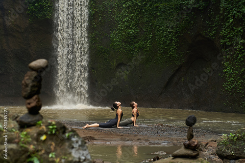 two young women doing yoga todether near the waterfall