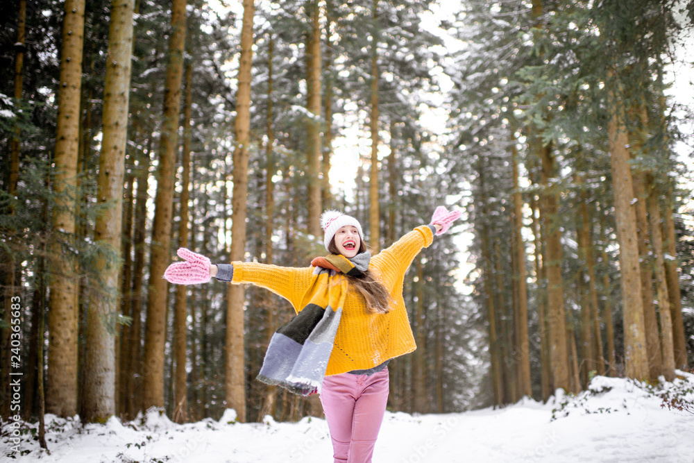 Portrait of a young playful woman dressed in bright winter clothes enjoying nature in the pine forest during the winter