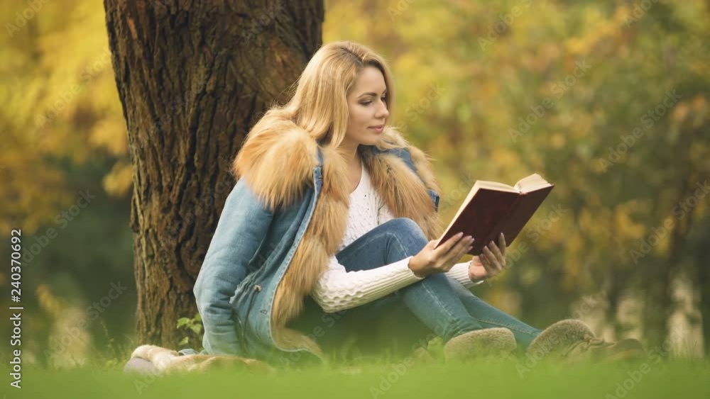 Beautiful woman reading bestseller as sitting under tree in autumn forest, hobby Beautiful woman reading bestseller as sitting under tree in autumn forest, hobby