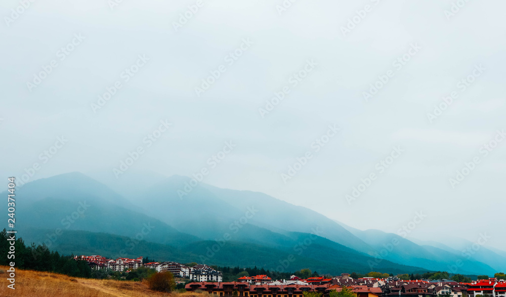 European alpine mountain village. Countryside, city near the hills in a morning fog, autumn.