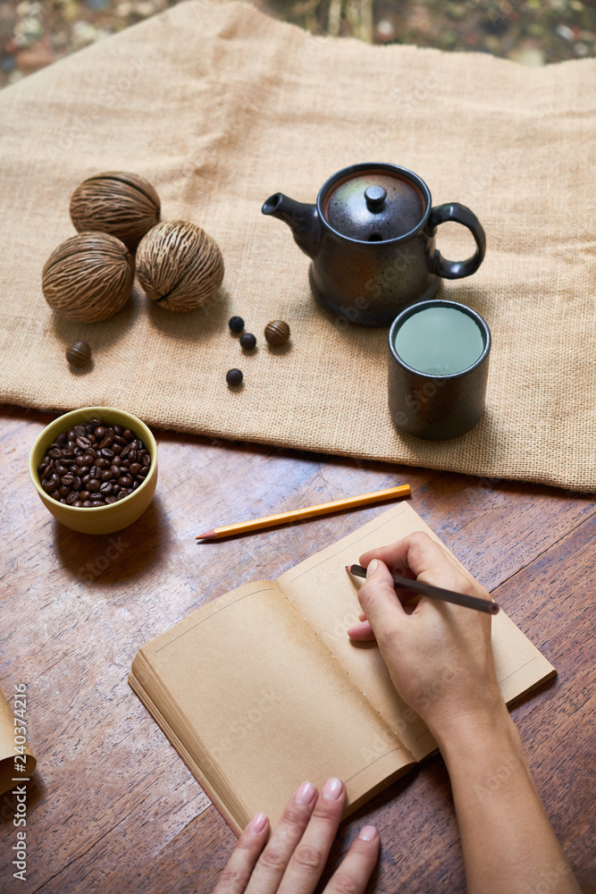 Fototapeta premium Top view of female hands making notes in notebook at the wooden table with cup of coffee