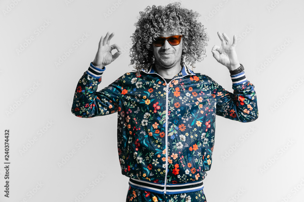 Adult positive smiling funky man with afro curly hair style in suglasses,  multicolored clothes making okay gesture with hands on white studio  background. Funny portrait of artistic stylish male person Stock Photo |