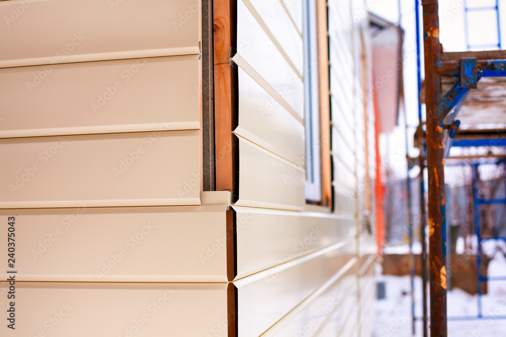 Close-up of house corner with beige siding covering walls and scaffolding. Close-up of house corner with beige siding covering walls and scaffolding.