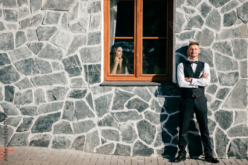 Fototapeta Naklejka Na Ścianę i Meble -  groom stands next to window where bride