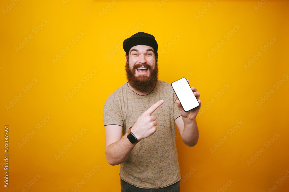 Happy young bearded man is pointing at white screen of smartphone Happy young bearded man is pointing at white screen of smartphone