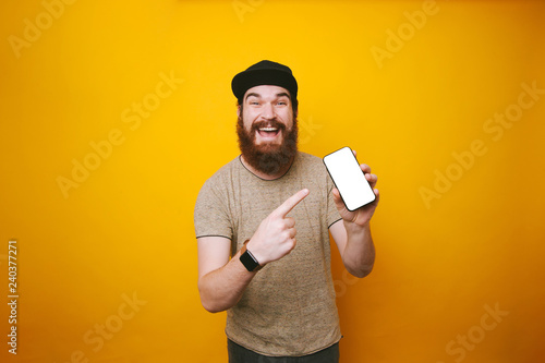 Happy young bearded man is pointing at white screen of smartphone