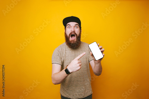 Amazed bearded man is holding and poiting at mobille white screen photo
