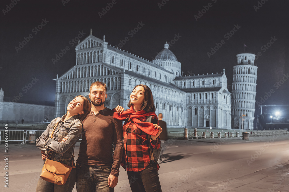 Obraz premium Group of tourists friends travel in Pisa, Italy, looking at the leaning tower and piazza dei miracoli at night time