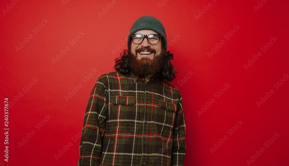 Hipster bearded man in hat and glasses, smiling, standing over red background Hipster bearded man in hat and glasses, smiling, standing over red background