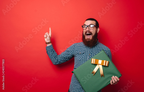 Cheerful bearded man holds his gist box and poiting up at copy space
