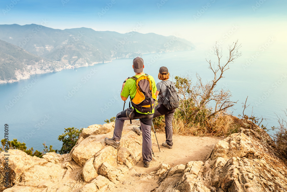 Happy couple hikers standing on top of the cliff and looking at the great seascape Happy couple hikers standing on top of the cliff and looking at the great seascape