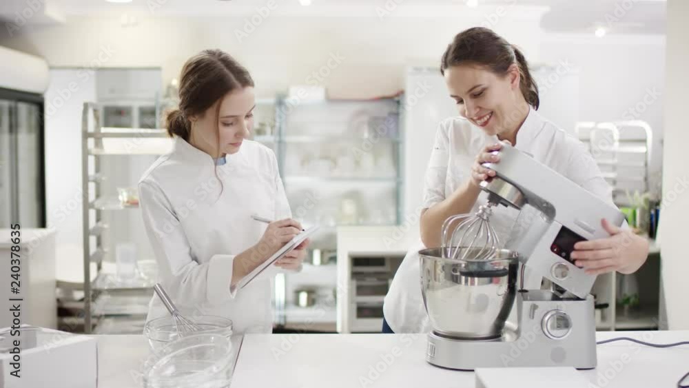Woman cook chef teaching lady sous chef to prepare dish and to use kitchen machines. Woman cook chef teaching lady sous chef to prepare dish and to use kitchen machines.