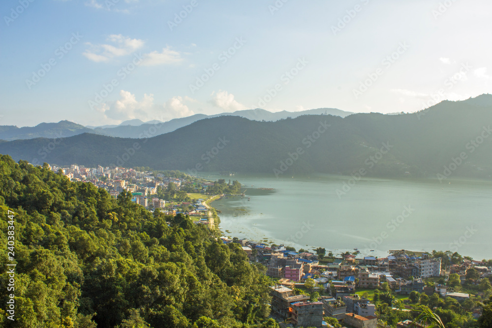 view of a huge mountain valley with a large city by the lake on the background of green wooded mountains