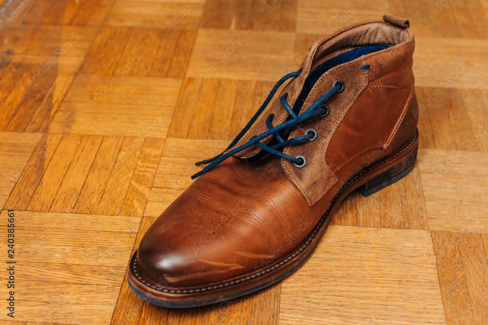close up of old brown leather shoe on wooden background close up of old brown leather shoe on wooden background
