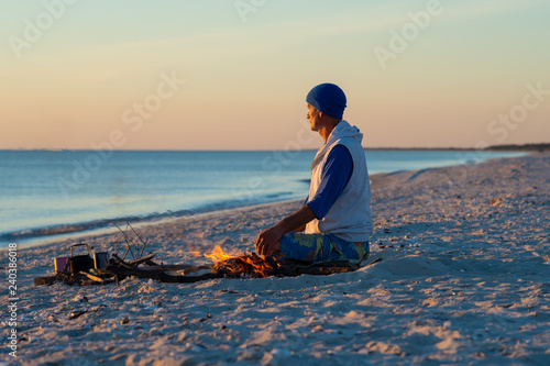 Traveler sits next to a bonfire on the seashore © sanechka