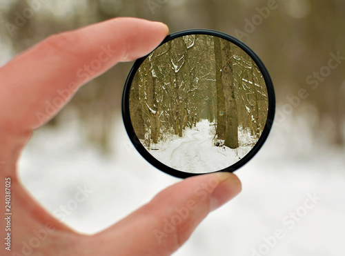 Hand holds a circular polarizer filter on winter landscape background. Winter season. Christmas,winter,snow. 