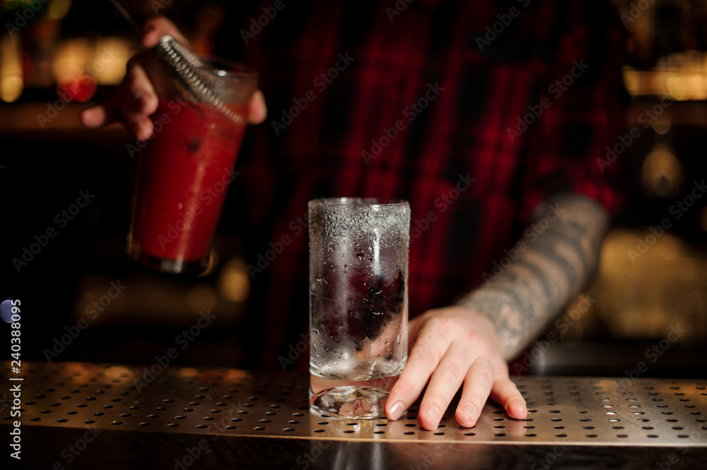 Bartender holding a glass of a Bloody Mary cocktail and the measuring cup