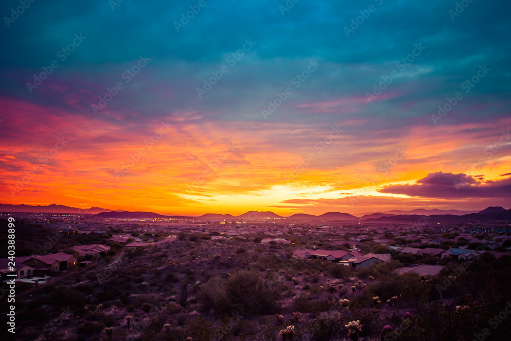A colorful sunset over a neighborhood in the desert of the American southwest. The sky has warm golden colors on the horizon with cool blue tones in the clouds at the top of the image.