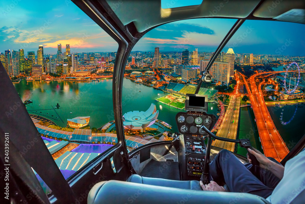Fototapeta premium Wnętrze kokpitu helikoptera na zmierzchu panorama zatoki mariny w Singapurze z oświetlonymi wieżowcami dzielnicy finansowej w centrum miasta. Widok z lotu ptaka gród Singapuru.