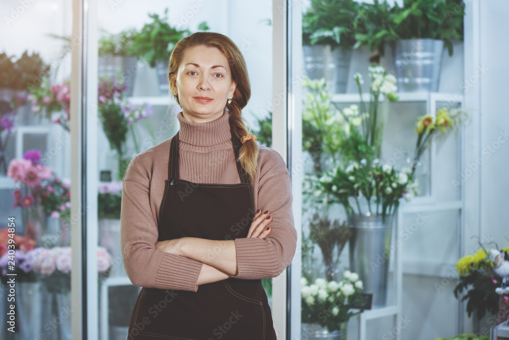 Florist woman in brown apron at flower salon in front of fridge with bouquets of flowers. Florist woman in brown apron at flower salon in front of fridge with bouquets of flowers.