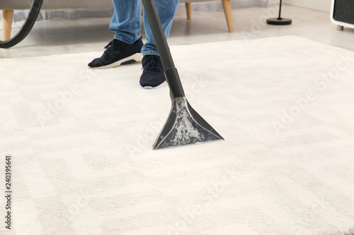 Man removing dirt from carpet with vacuum cleaner indoors, closeup