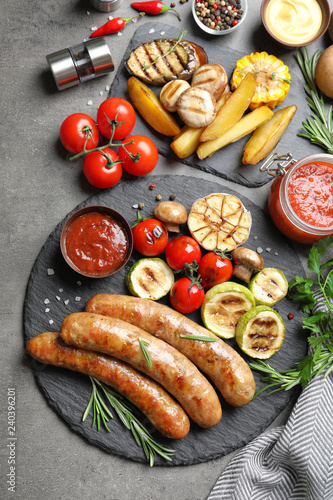 Delicious sausages and vegetables served for barbecue party on gray background, top view
