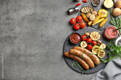 Flat lay composition with delicious barbecued sausages and vegetables on gray background. Space for text