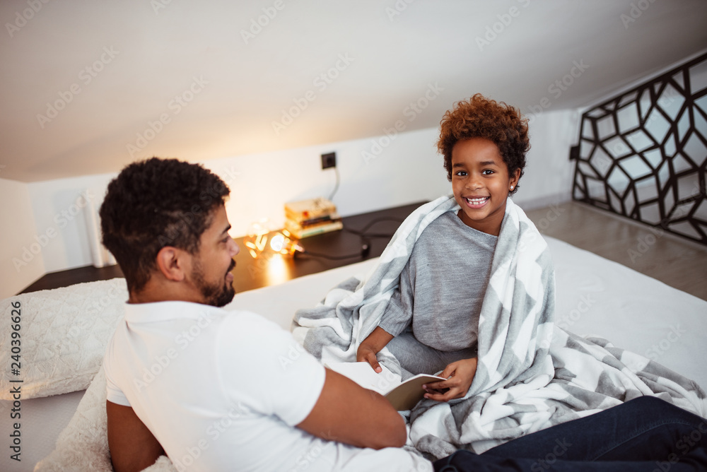 Fototapeta premium Dad and daughter reading a book together on bed.