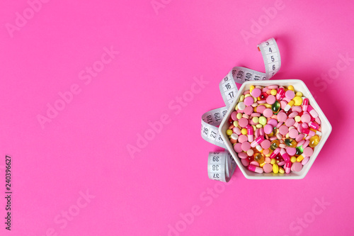 Bowl with weight loss pills and measuring tape on color background, top view. Space for text