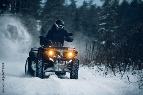 Rider driving in the quadbike in winter in the forest . Biker go fast at the winter forest with a splashes of ice 