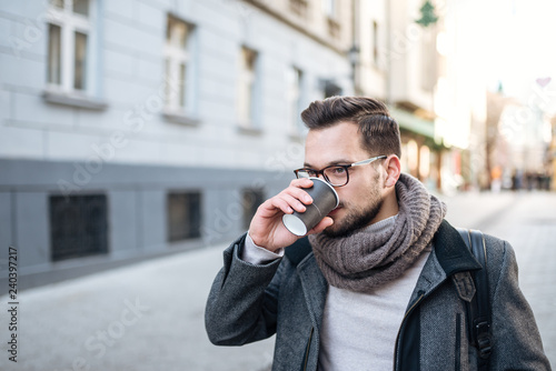 Close-up image of young man walking and drinking coffee in the city street.