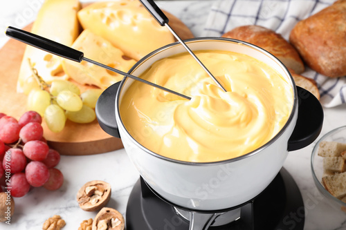 Pot of delicious cheese fondue and forks on table
