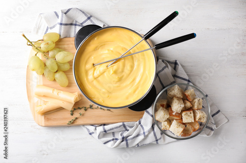 Flat lay composition with pot of delicious cheese fondue on wooden table