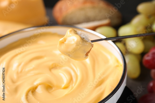Piece of bread over pot with delicious cheese fondue  closeup
