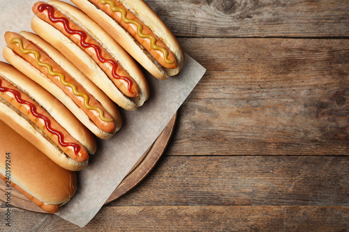 Fotografia Tasty fresh hot dogs on wooden table, top view. Space for text