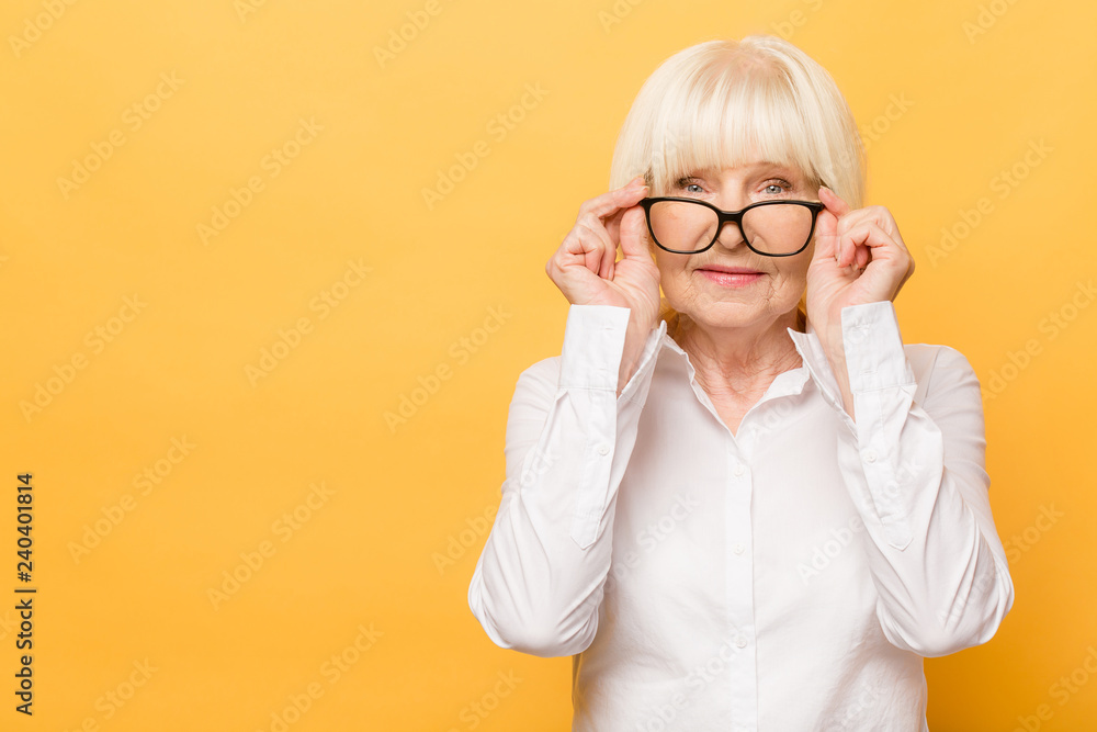 Joyful senior lady in glasses laughing isolated over yellow background. Friendly, mature white haired woman wearing glasses with a smile. Joyful senior lady in glasses laughing isolated over yellow background. Friendly, mature white haired woman wearing glasses with a smile.