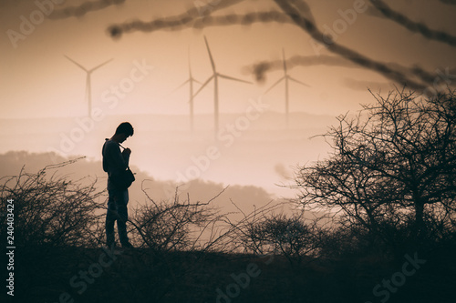 Silhouette of a man looking down with windmills in the background