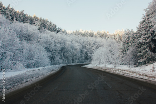 Beautiful snow-covered road through the forest. On the sides of the road trees in the white fluffy snow.