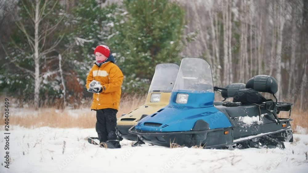 Winter forest. A little boy standing by the snowmobile and making a snowball. Slow motion Winter forest. A little boy standing by the snowmobile and making a snowball. Slow motion