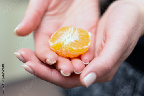 The girl holds a piece of mandarin in her hands. Hands of a girl with a beautiful manicure_