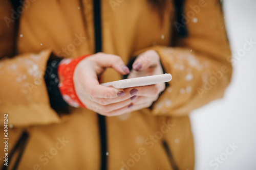 Hands holding smartphone with glowing screen. Hipster girl texting message on smartphone mobile in winter nature © uflypro