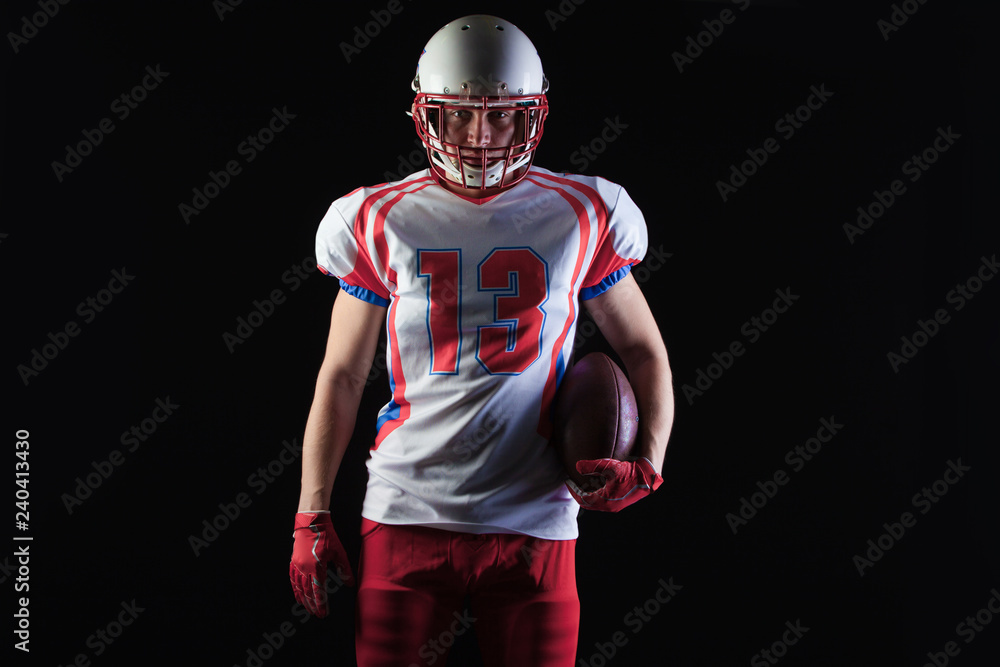American football player wearing helmet posing with ball on black background