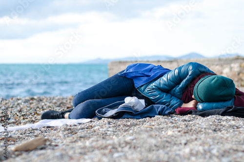 A homeless girl wrapped in clothes sleeps on the beach. Homeless concept. Athens, Greece