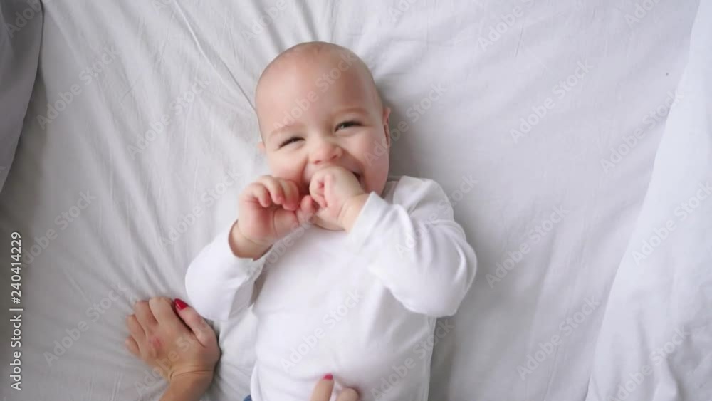 Baby in white t-shirt lying on a white bed and laughing looking at the camera top view slow motion Baby in white t-shirt lying on a white bed and laughing looking at the camera top view slow motion