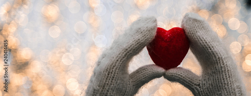 Female hands in knitted white mittens with heart of snow in winter day. Love and St. Valentine cozy concept, copyspace, bokeh background, banner