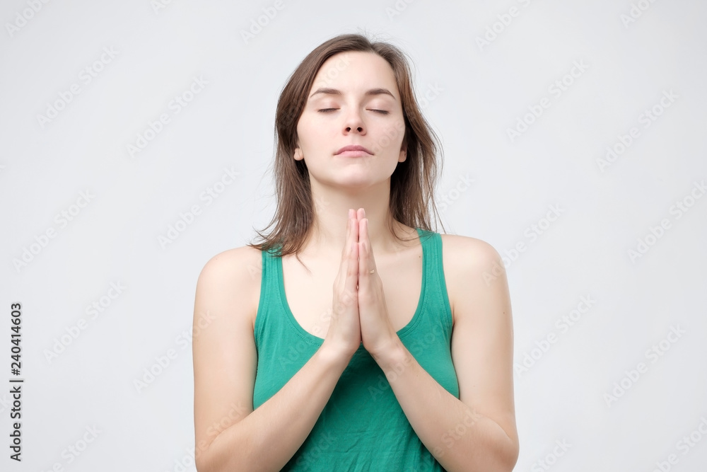 Female in green t-shirt prays for wellness of her family, keeps palms pressed together, eyes closed, poses in praying gesture. People, faith, hope, believe Female in green t-shirt prays for wellness of her family, keeps palms pressed together, eyes closed, poses in praying gesture. People, faith, hope, believe