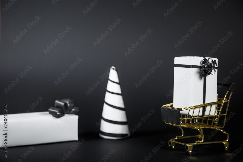White Christmas tree and gift in shop cart isolated on black background.